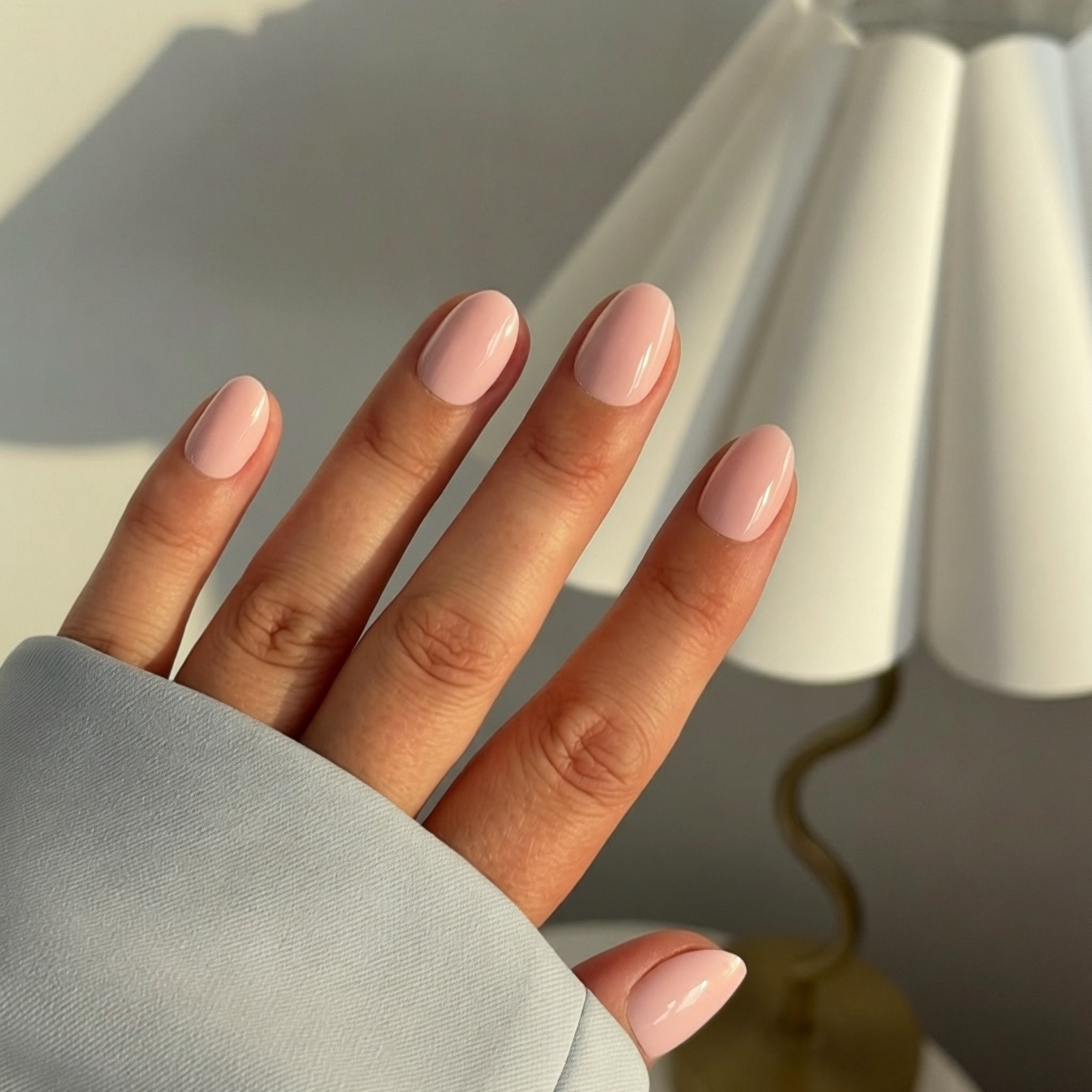 Hand wearing Instant Mani Co. light pink press on nails in front of lamp