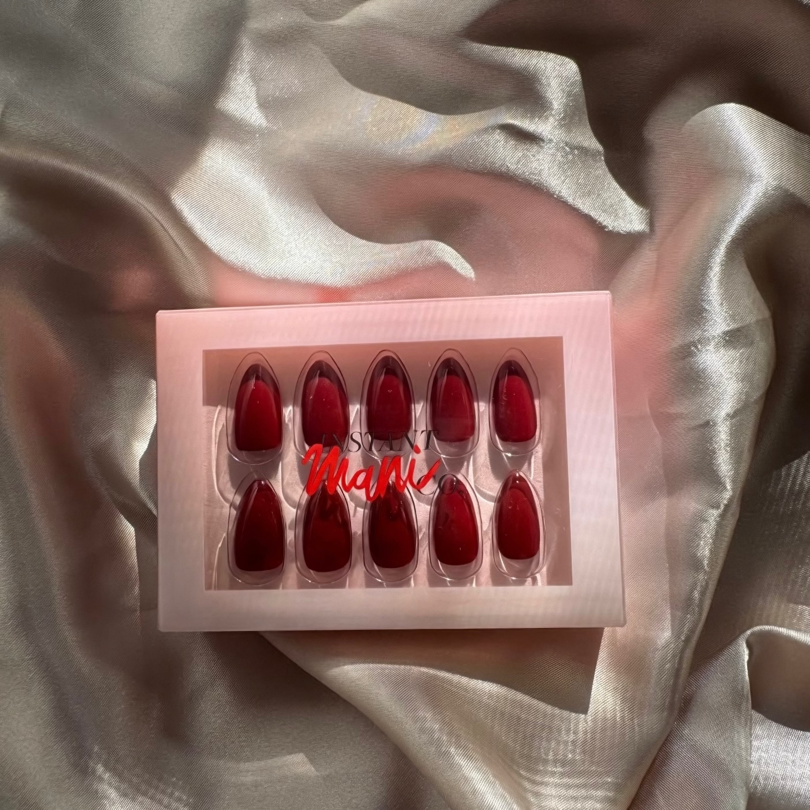 Set of rogue red Instant Mani Co. Press on nails in a box on a textured fabric background