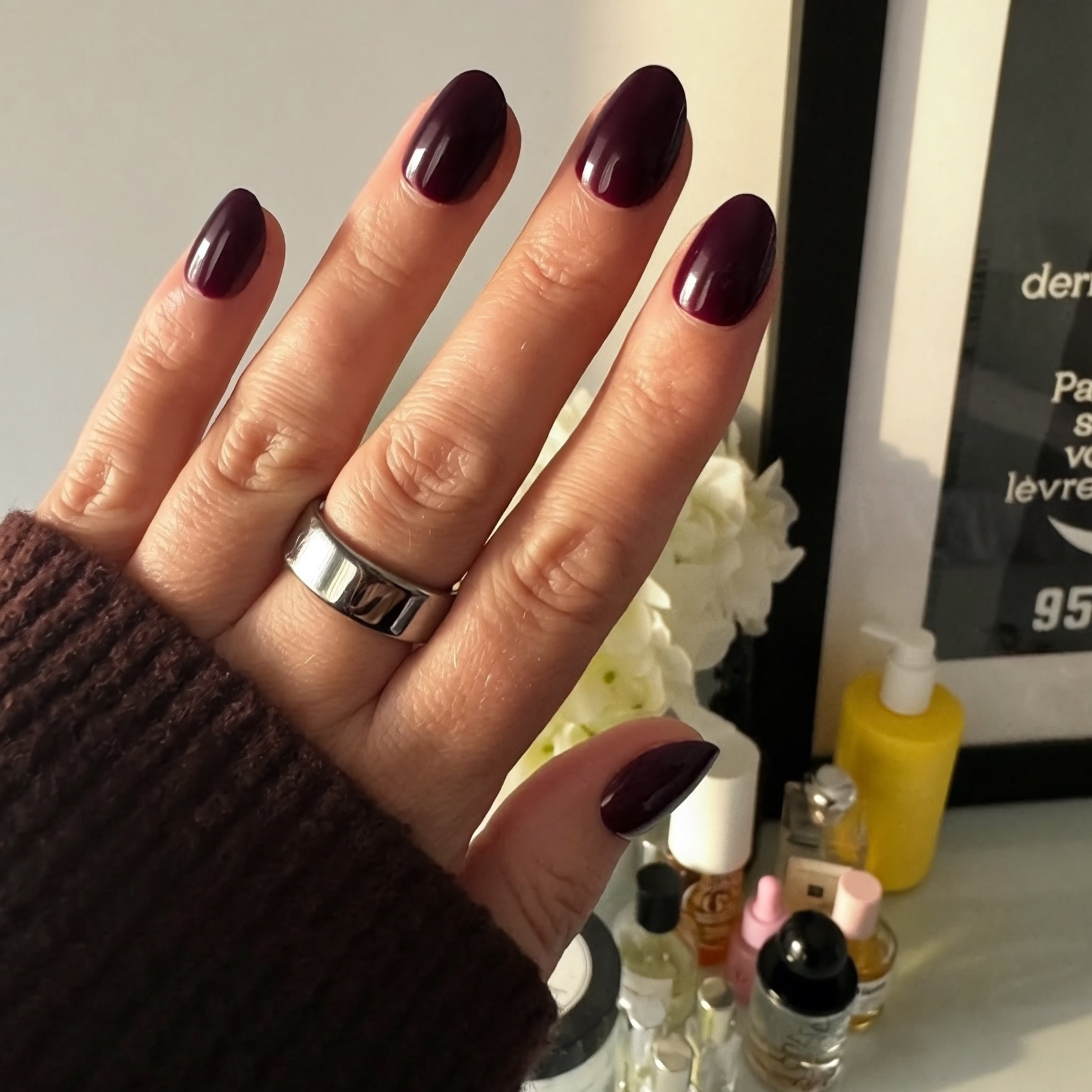 Hand with plum Instant Mani Co press on nails with a blurred background of beauty products.