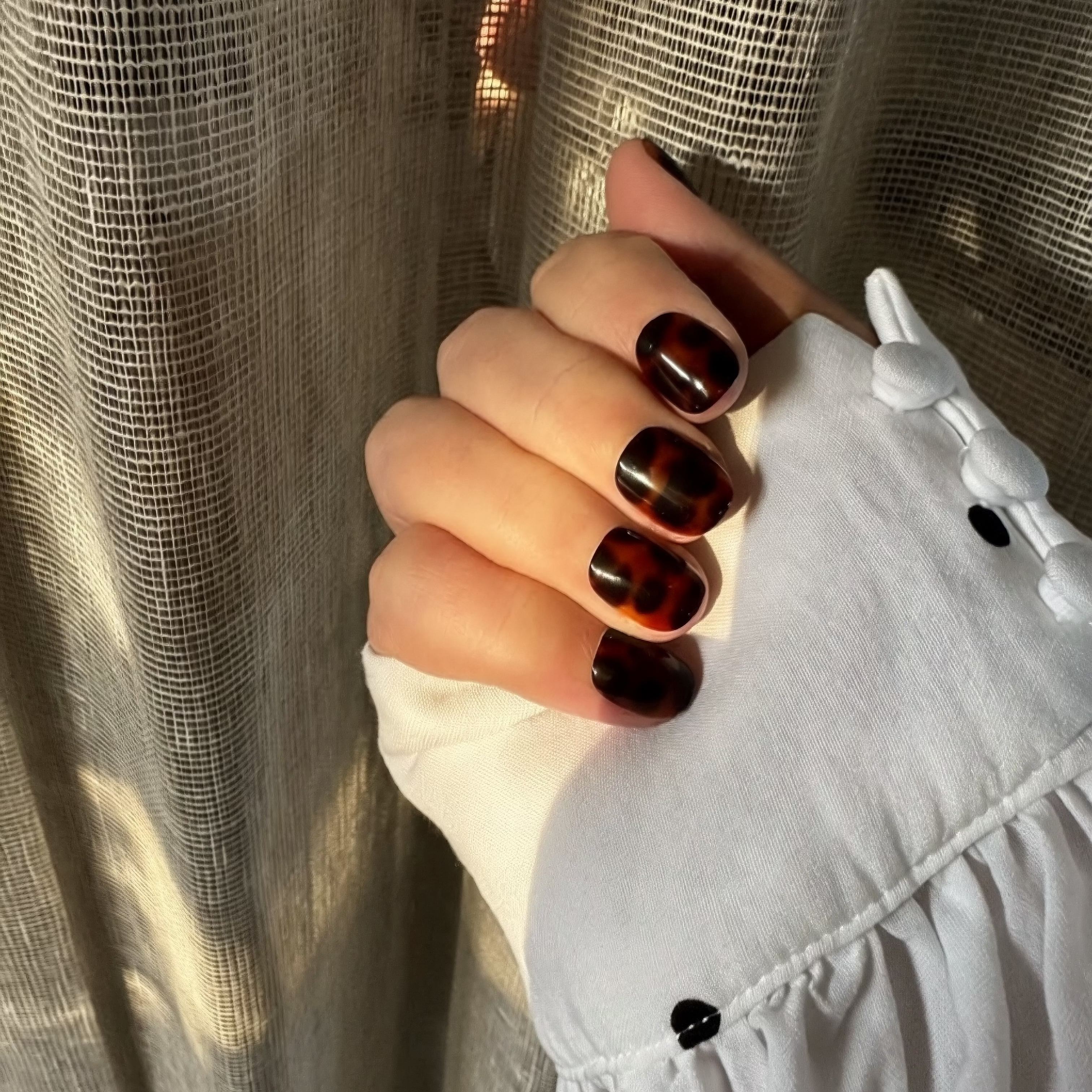Hand with tortoiseshell Instant Mani press on nails against a textured beige background