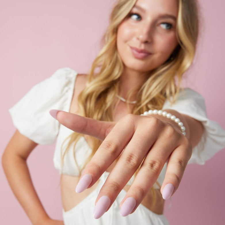 Girl wearing Instant Mani Co Velvet Pink Press on nails standing in front of pink background wearing white shirt