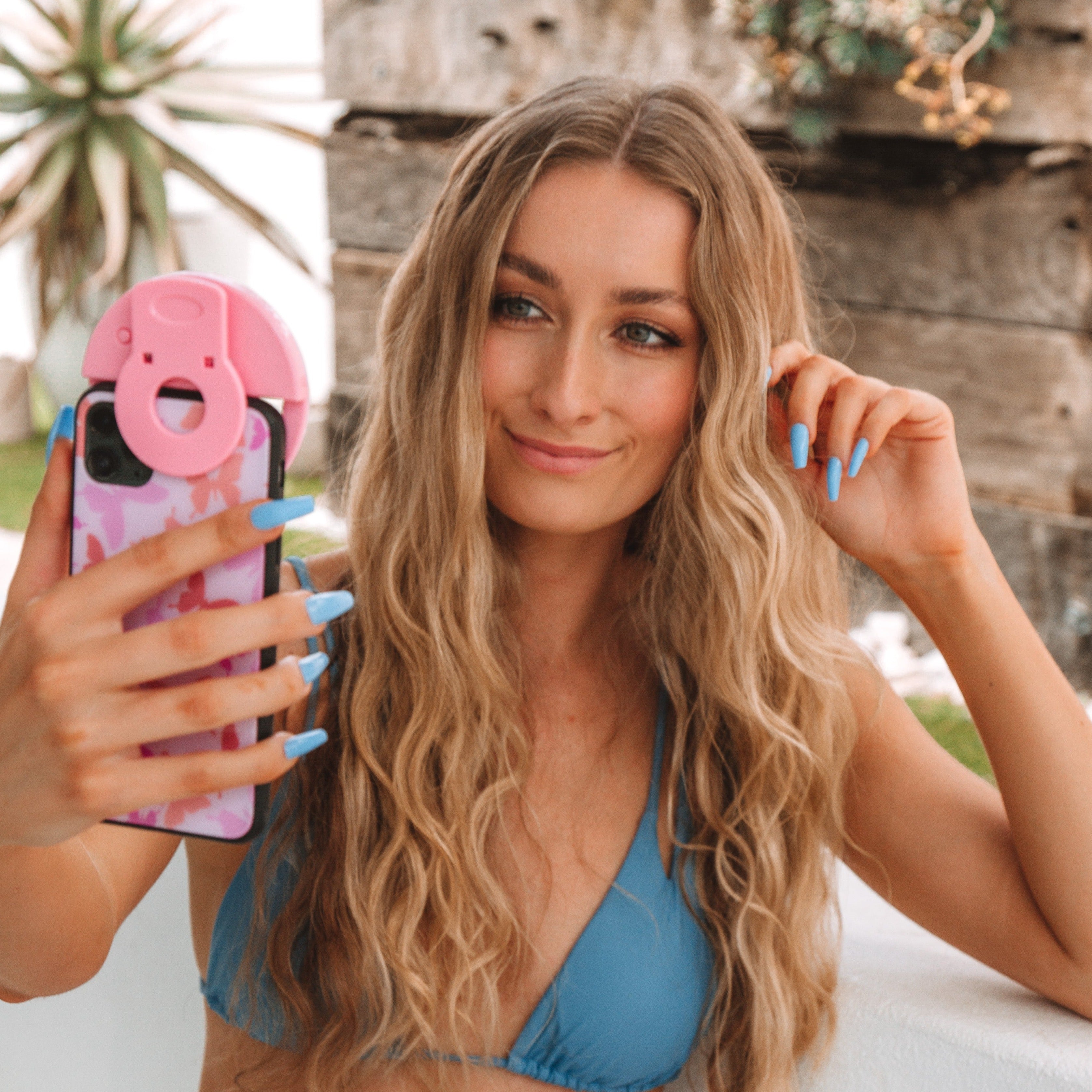 Girl taking a nailfie on her phone while wearing blue bikini, and blue press-on nails by Instant Mani Co
