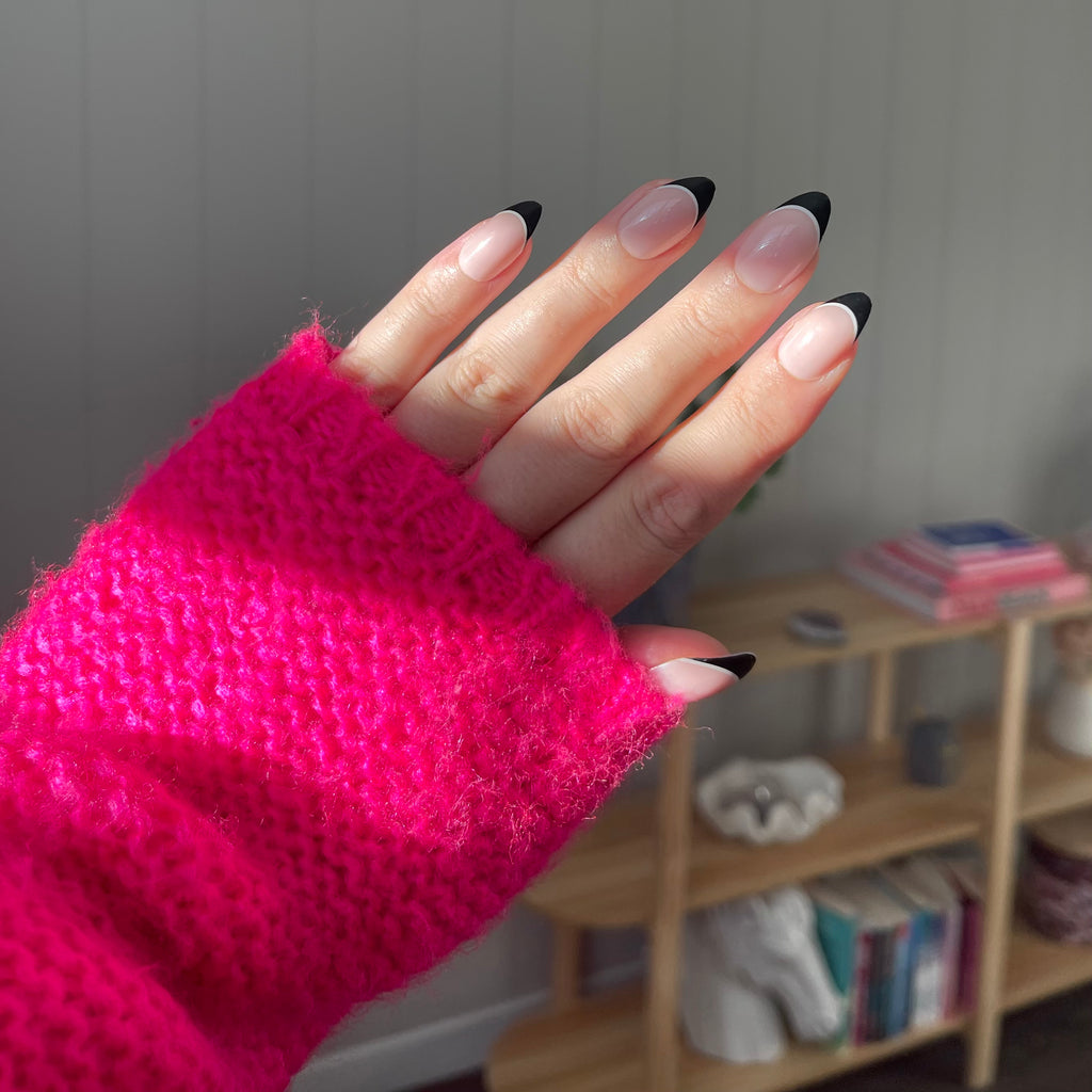 Girl wearing pink jumper and a set of Instant Mani Co. Swipe Right, black tip press on nails in the sunlight