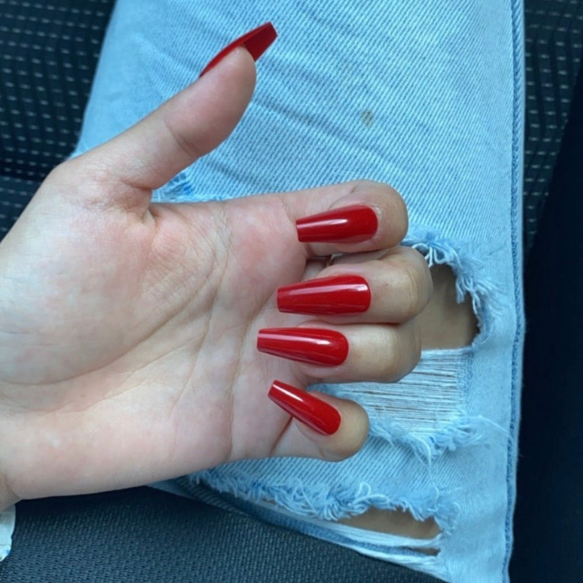 Girl with ripped jeans, wearing red Instant Mani Co press-on nails.