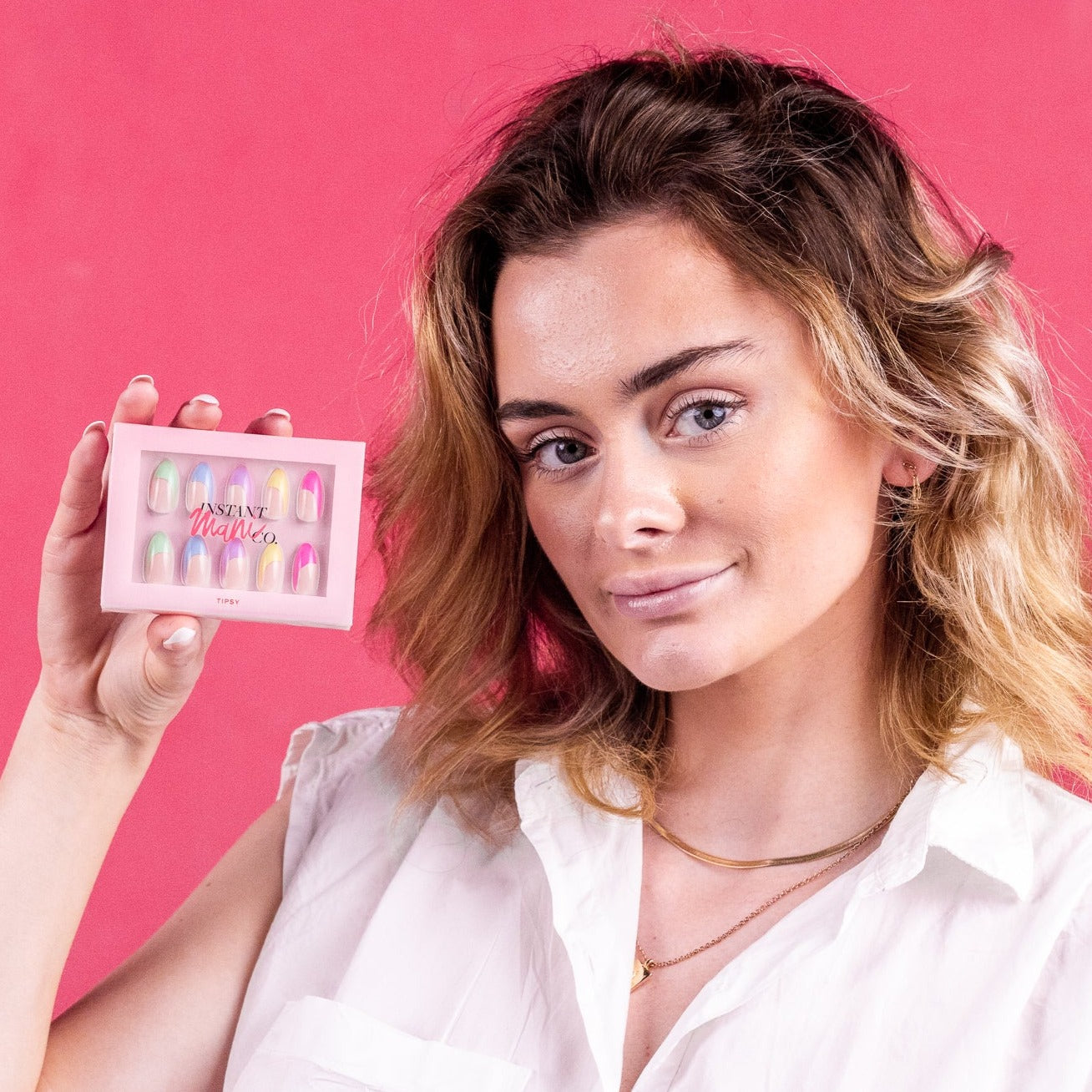 Girl smiling in front of pink background, holding a set of Instant Mani Co. Tipsy press-on nails