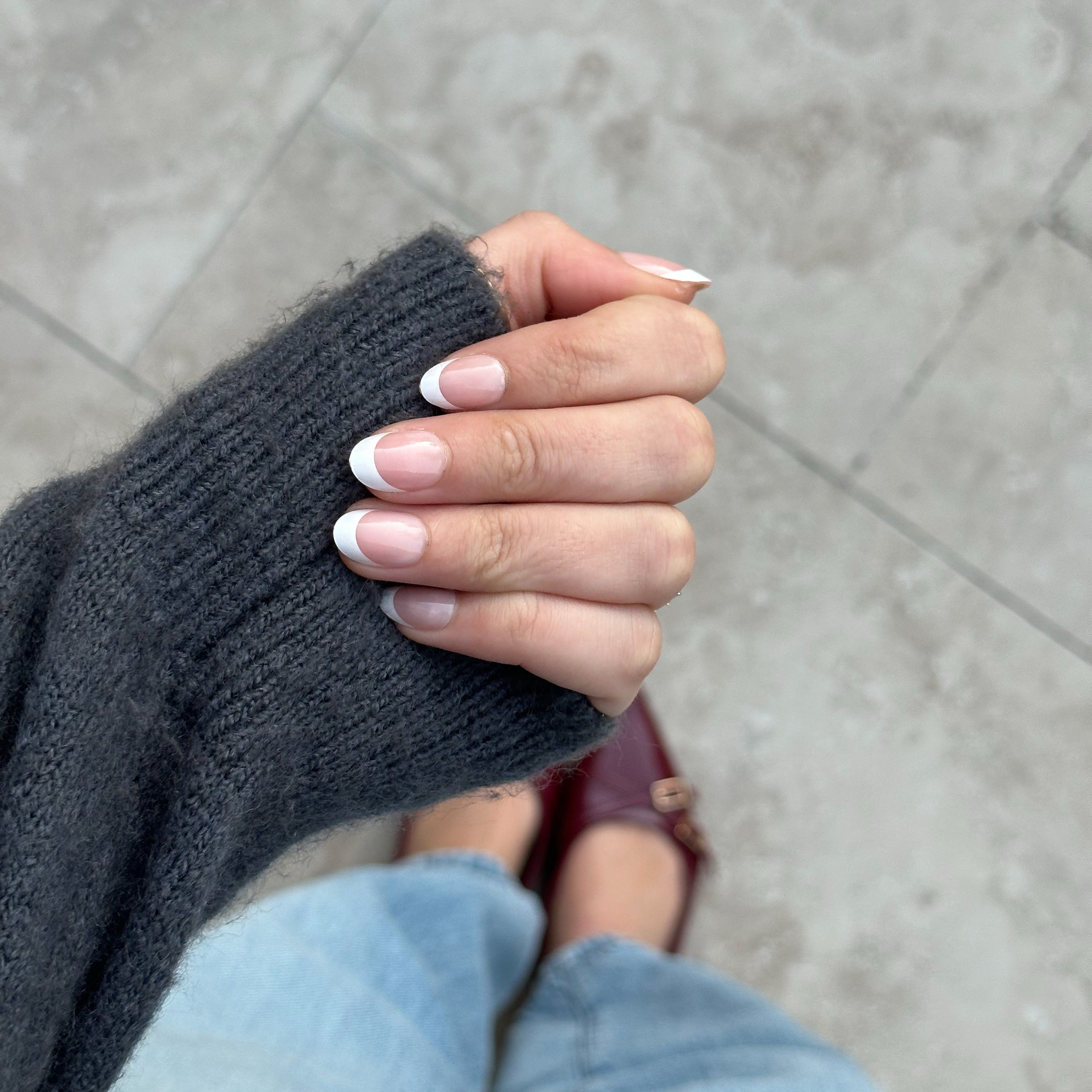 Hand wearing a dark gray sleeve with light gray pavement in the background, wearing instant mani co. press on nails