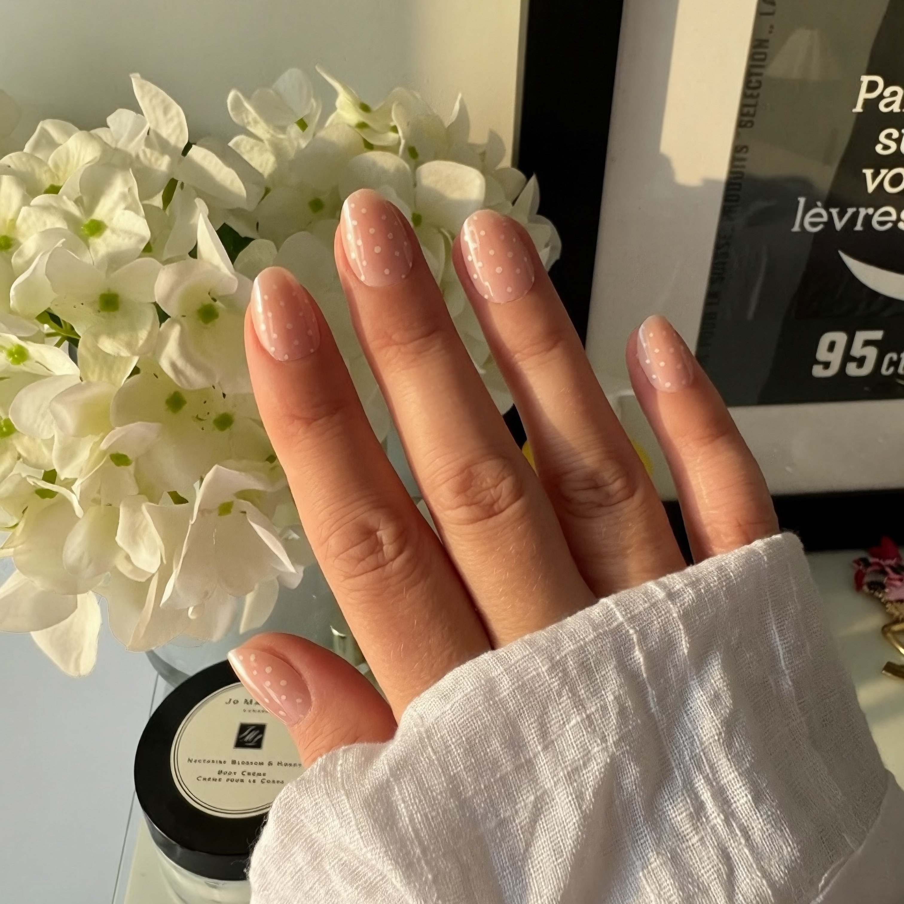 Hand wearing Instant Mani Co. polka dot press on nails with flowers and skincare in background