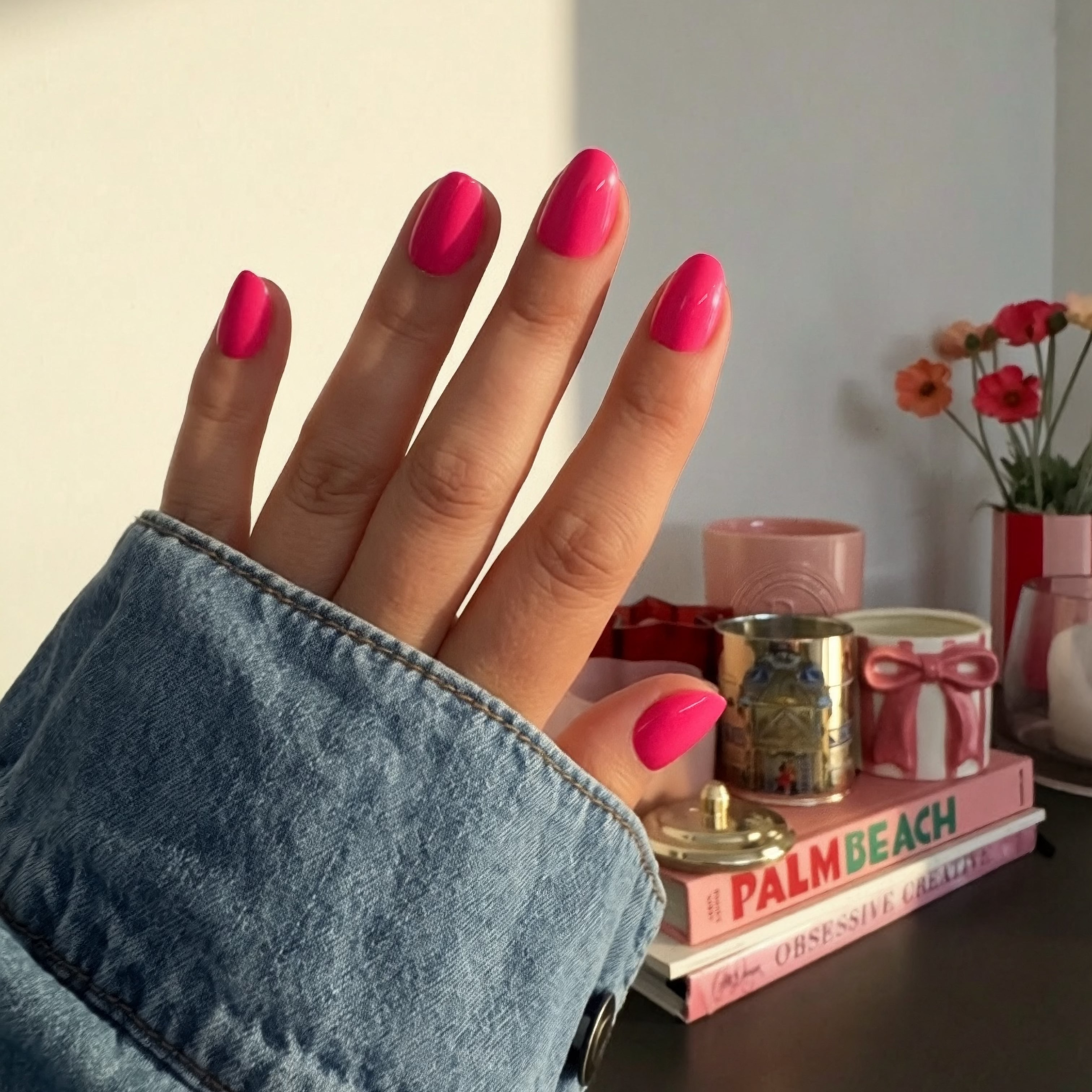 Hand with hot pink Barbie Instant Mani Co. press on nails on, with books and decor in background 