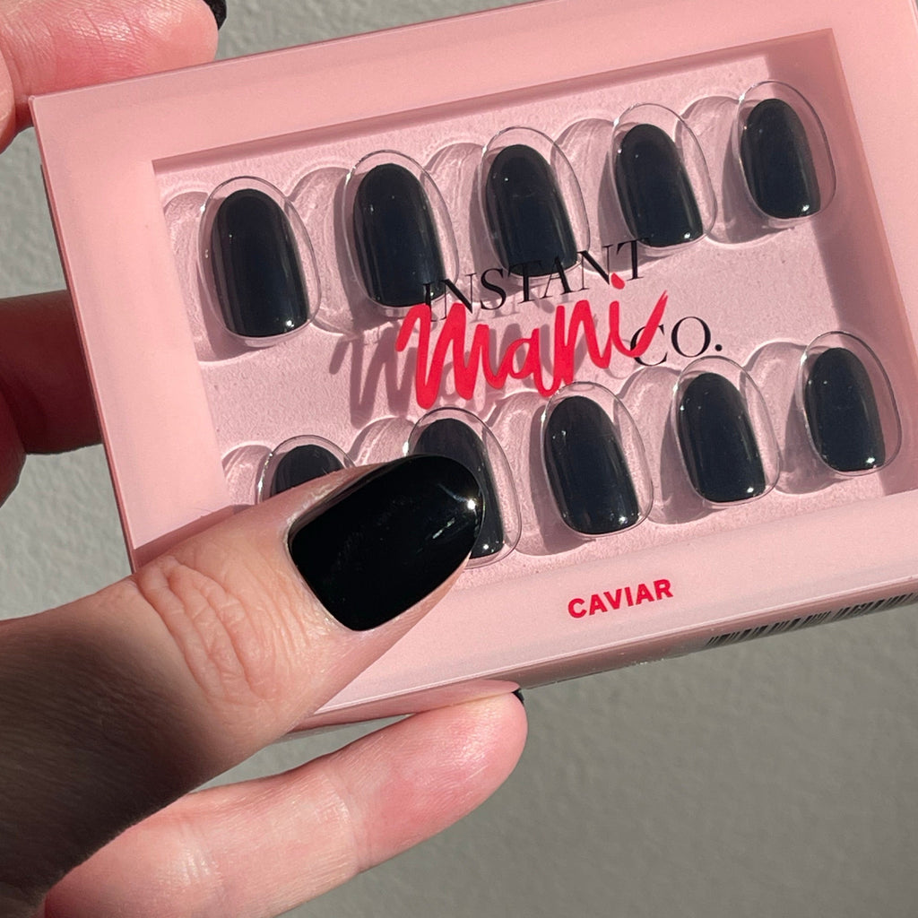 Girl wearing Instant Mani Co caviar black press on nails, holding set of nails in the sun