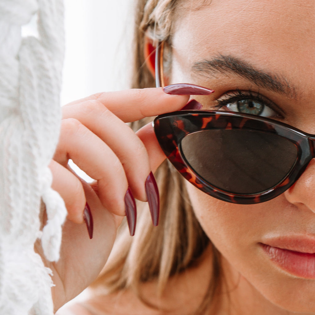  Close up shot of girl holding tortoiseshell sunglasses, wearing an Instant Mani press-on set of fake nails 