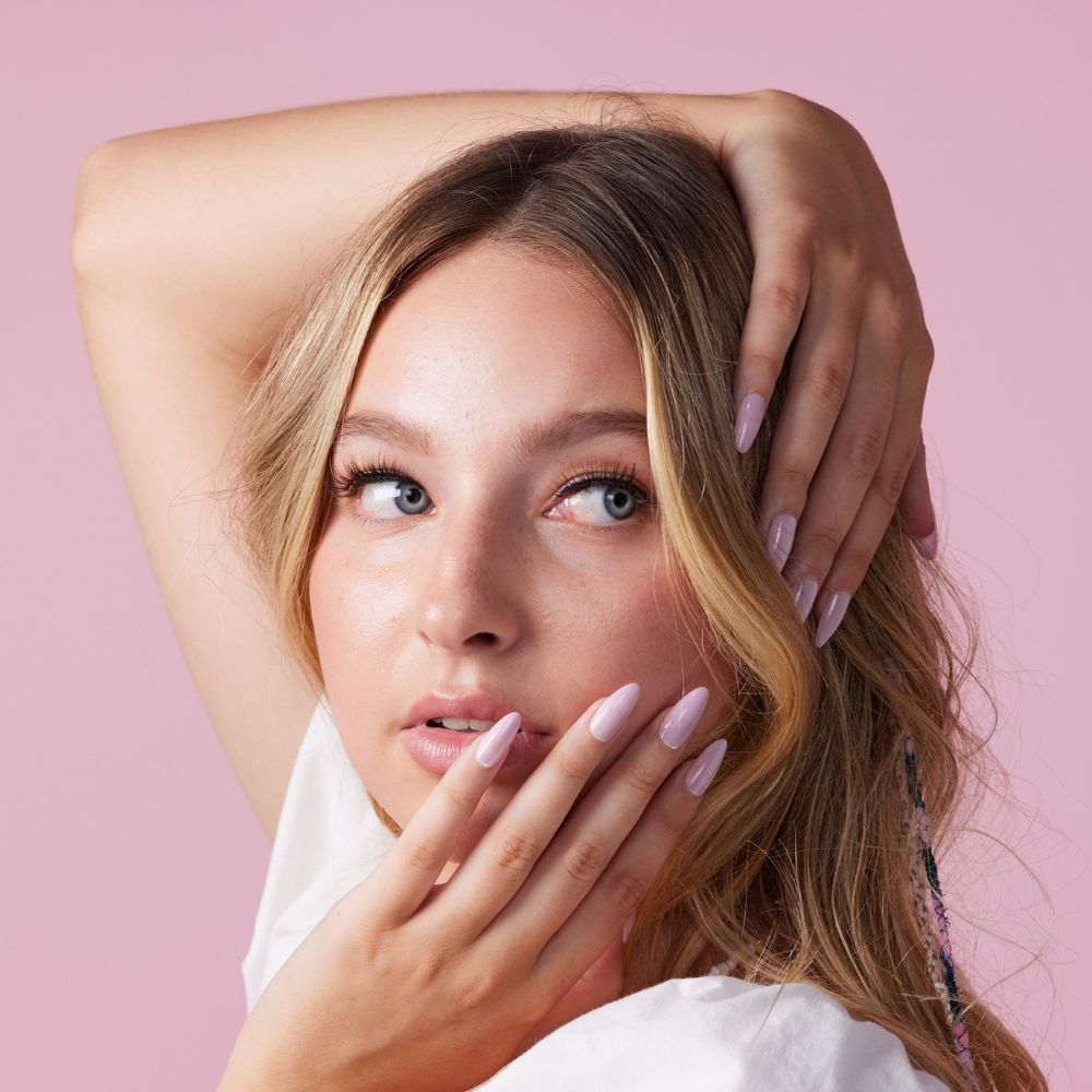 Girl wearing Instant Mani Co Velvet Pink Press on nails standing in front of pink background wearing white shirt 