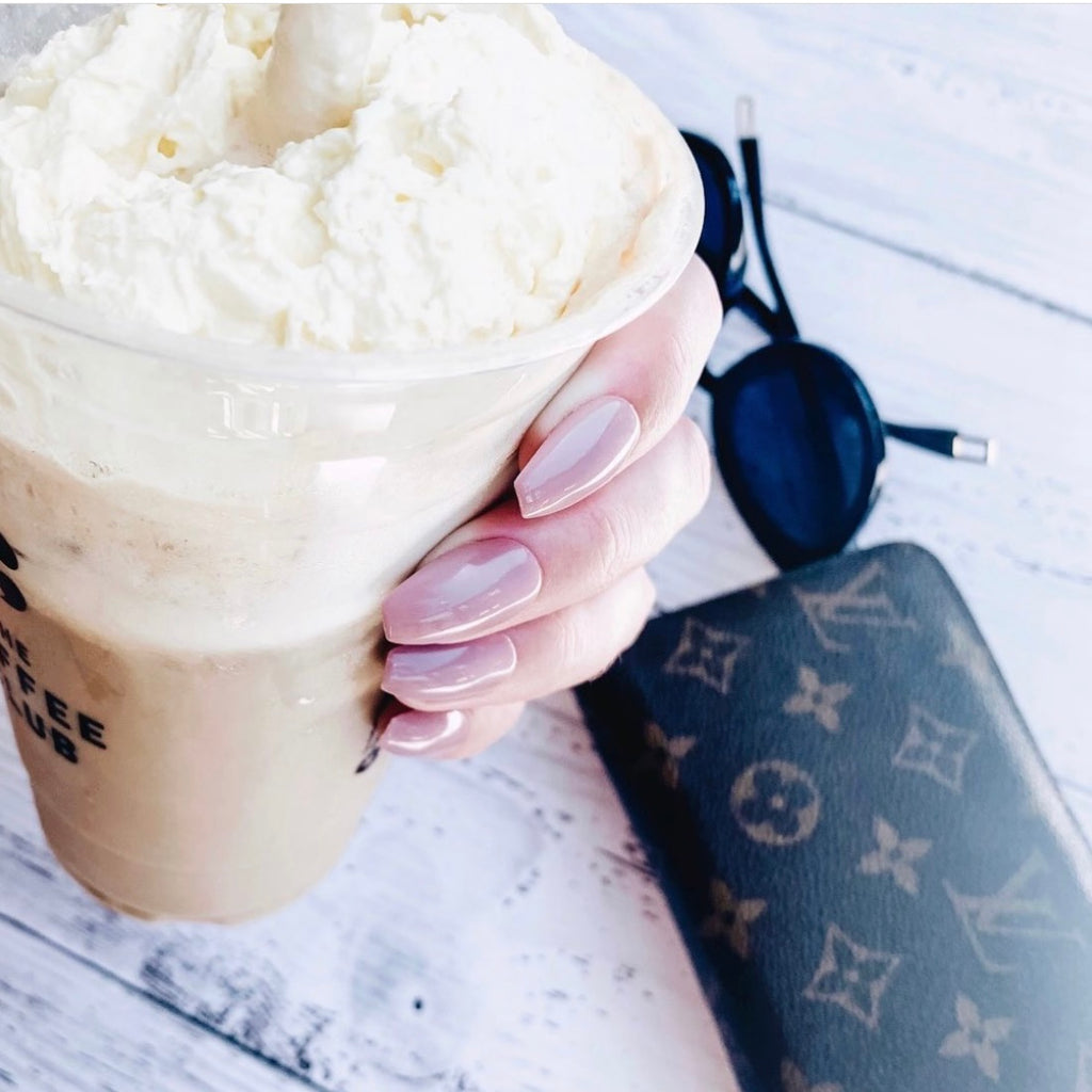 Girl holding ice coffee wearing nude press-on nails by Instant Mani Co with Louis Vuitton wallet in background