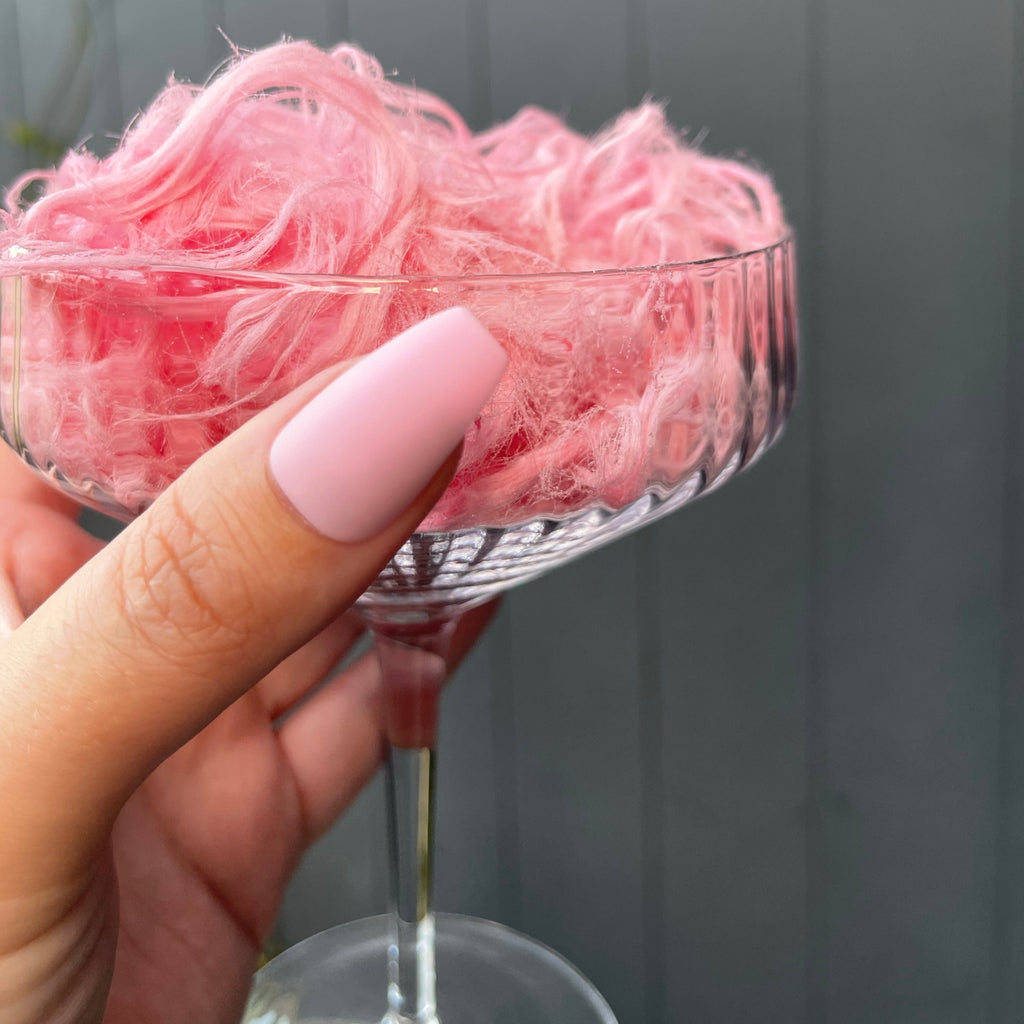 Hand holding champagne glass, wearing Instant Mani Co matte pink Flossy nails 