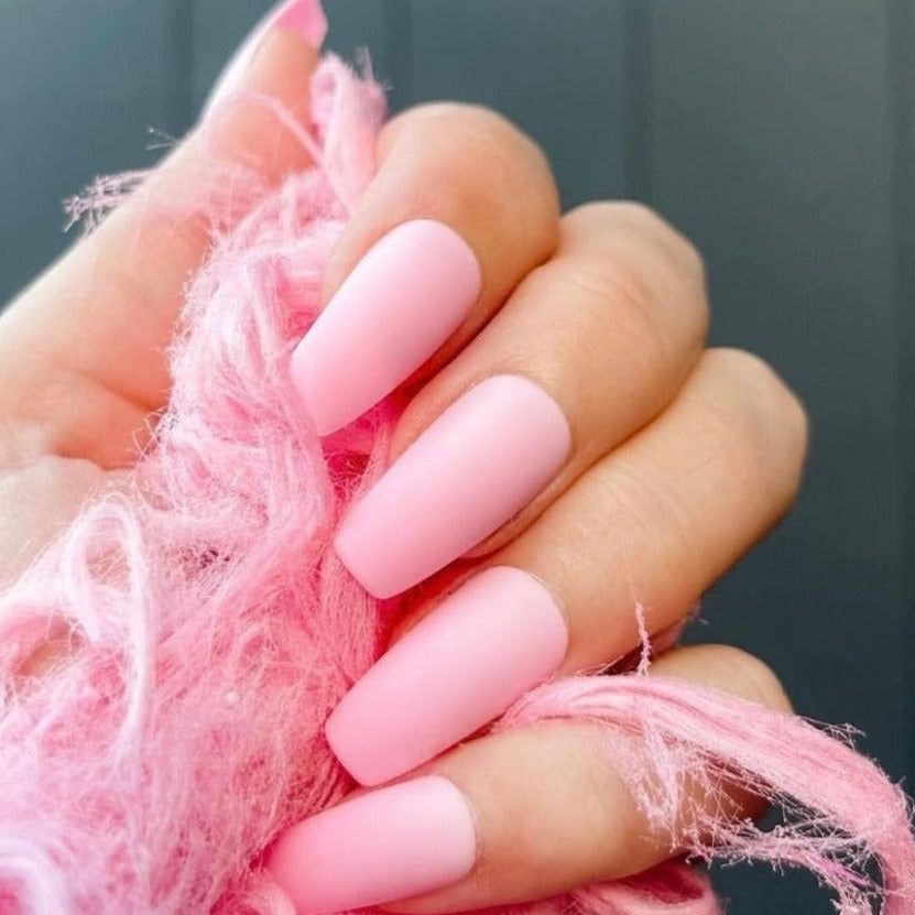 hand wearing Instant Mani Co. pink matte Flossy nails, holding fairy floss. 