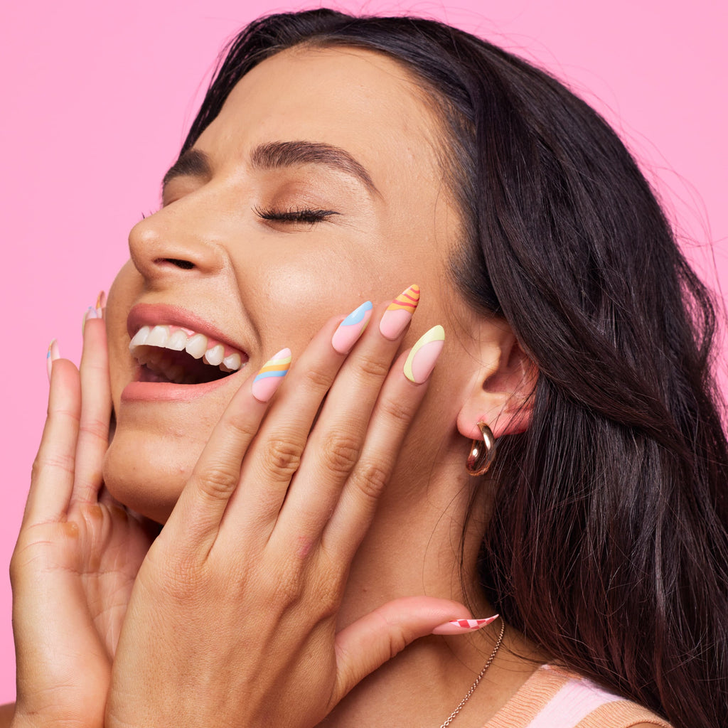 Girl smiling standing in front of pink background wearing Instant Mani Co. Carnival colourful press on nails. 