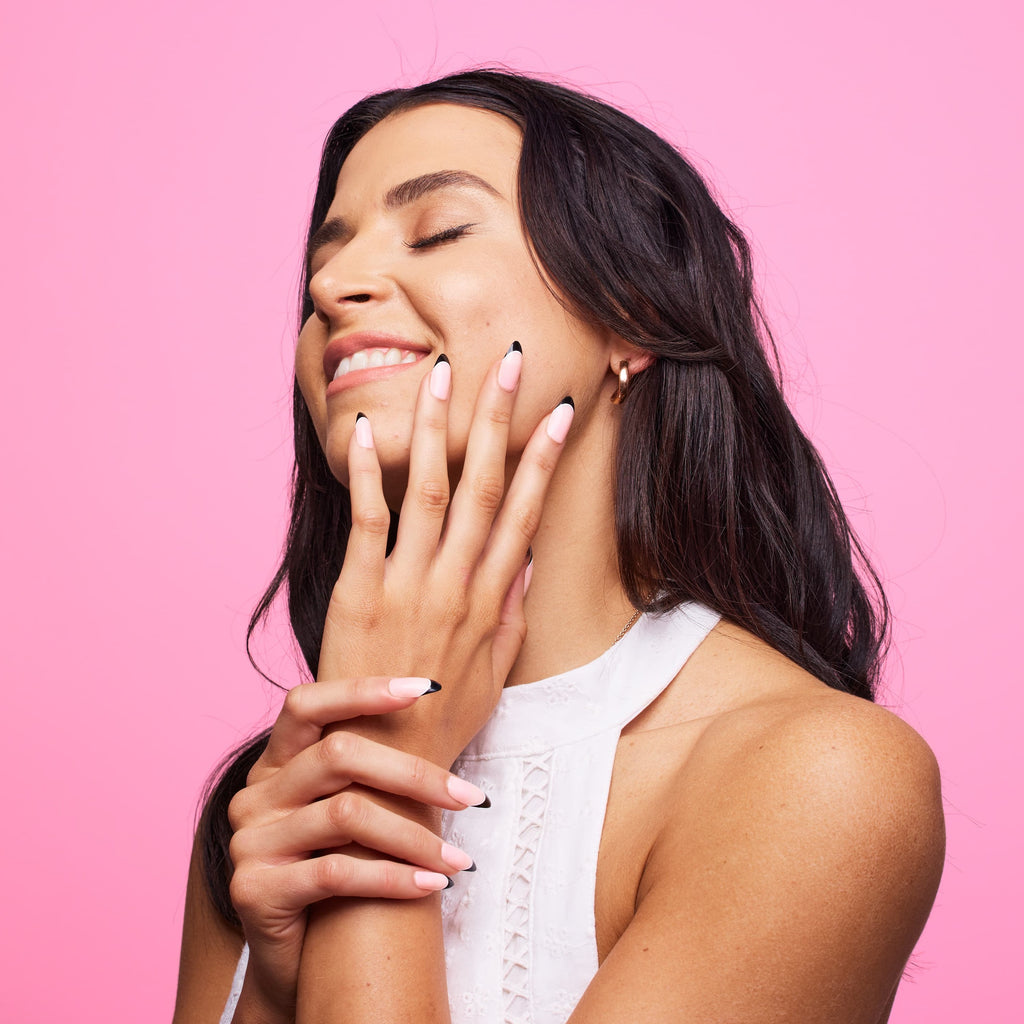 Girl in front of pink wearing black tipped Instant Mani Co. press on nails 