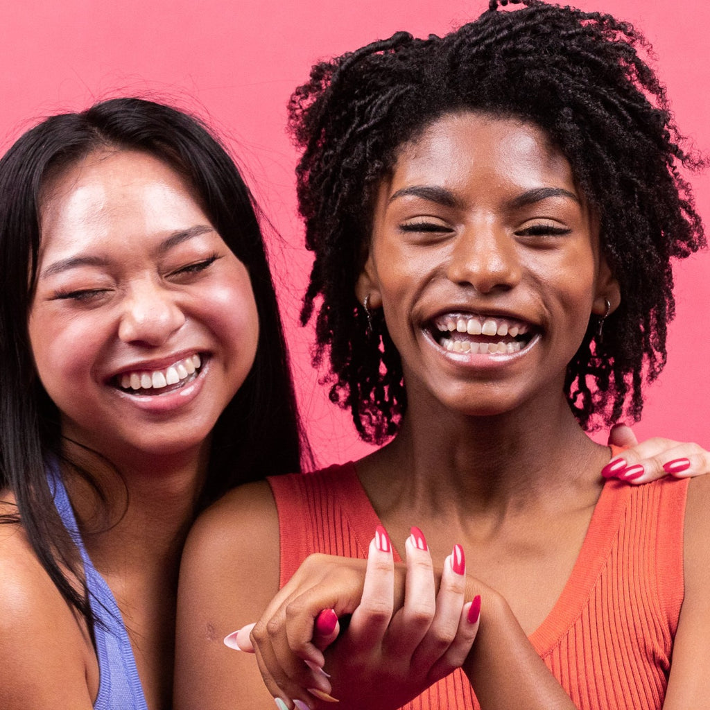 Two girls smiling, in front of pink background, wearing Instant Mani co. press-on nails