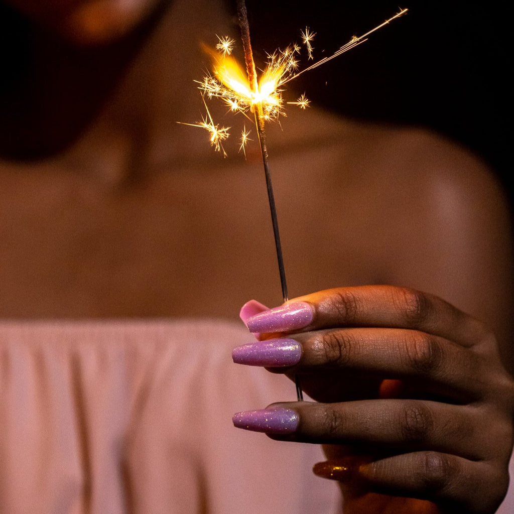 Close up of girl holding sparkler, while wearing pink glitter press on nails 
